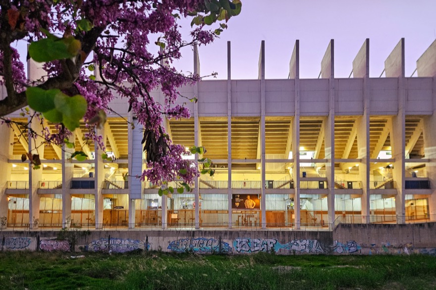 Estadio La Rosaleda, Málaga, as seen from the east from the footpath on the other side of the Río Guadalmedina, partly framed by blossoms. The stadium lights ar