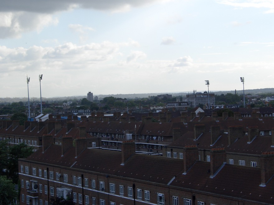 Os refletores de Loftus Road aparecendo por cima dos telhados de Shepherd's Bush, o estádio espremido entre as casas.